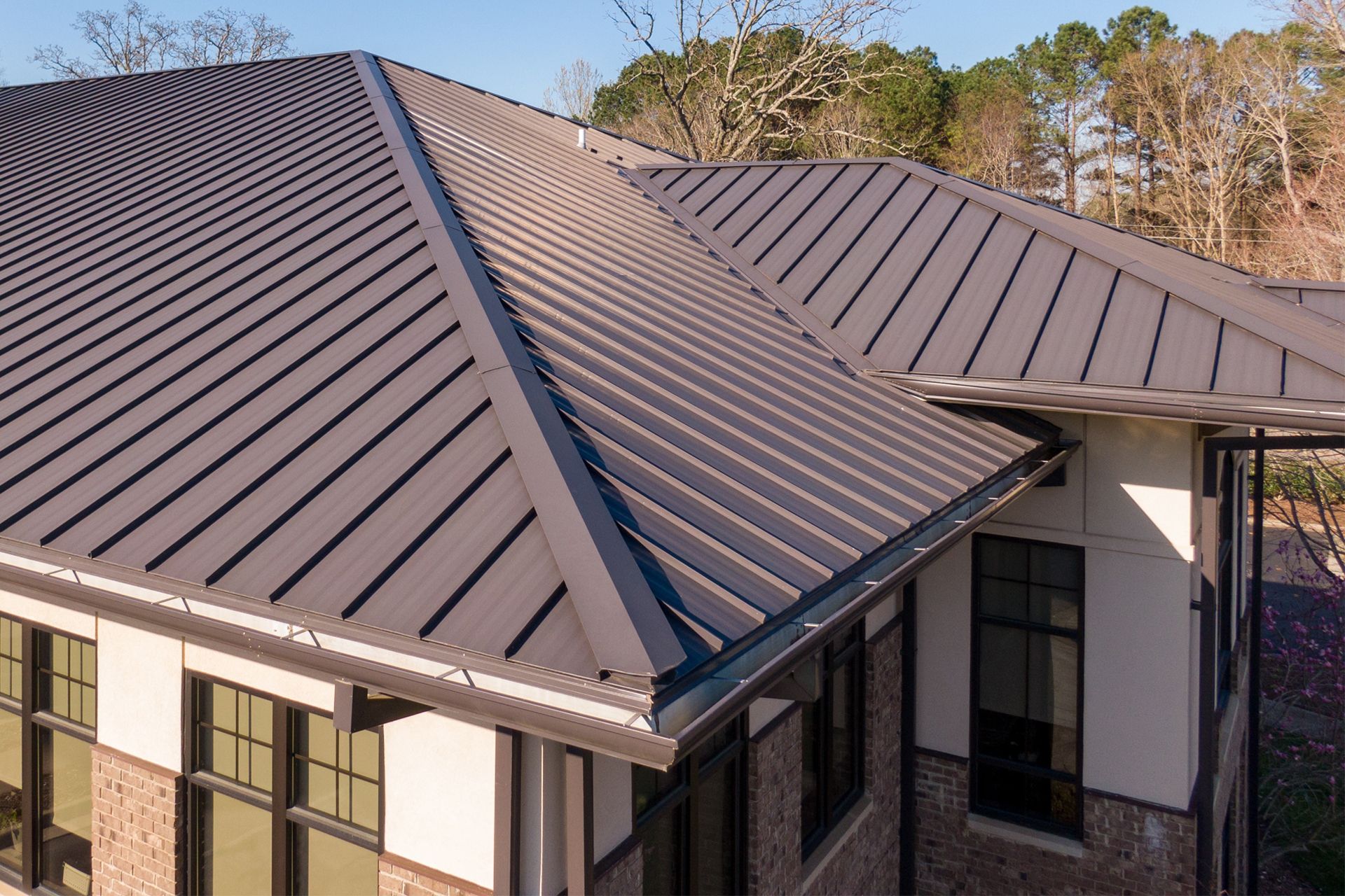 An aerial view of a dark brown metal standing-seam roof on a modern building with stone and white walls.