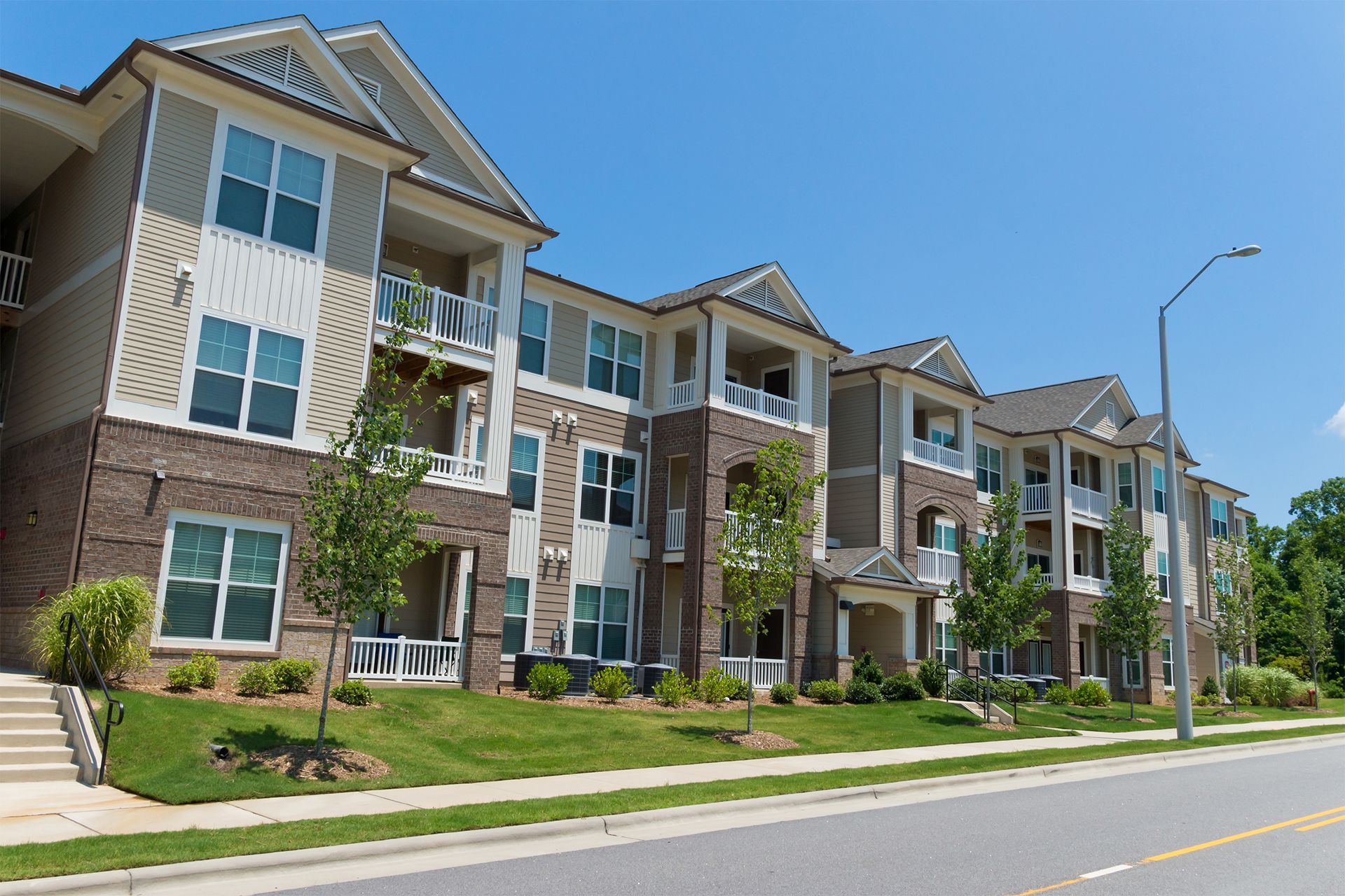 A modern apartment complex with tan siding and brick accents under a clear blue sky.