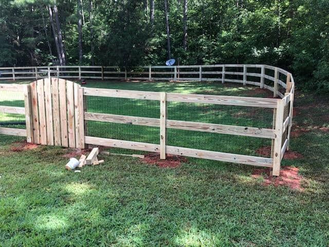 A wooden fence with a gate in the middle of a lush green field.