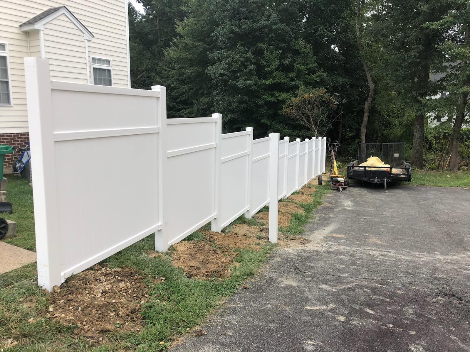 A white vinyl fence is being installed in front of a house.
