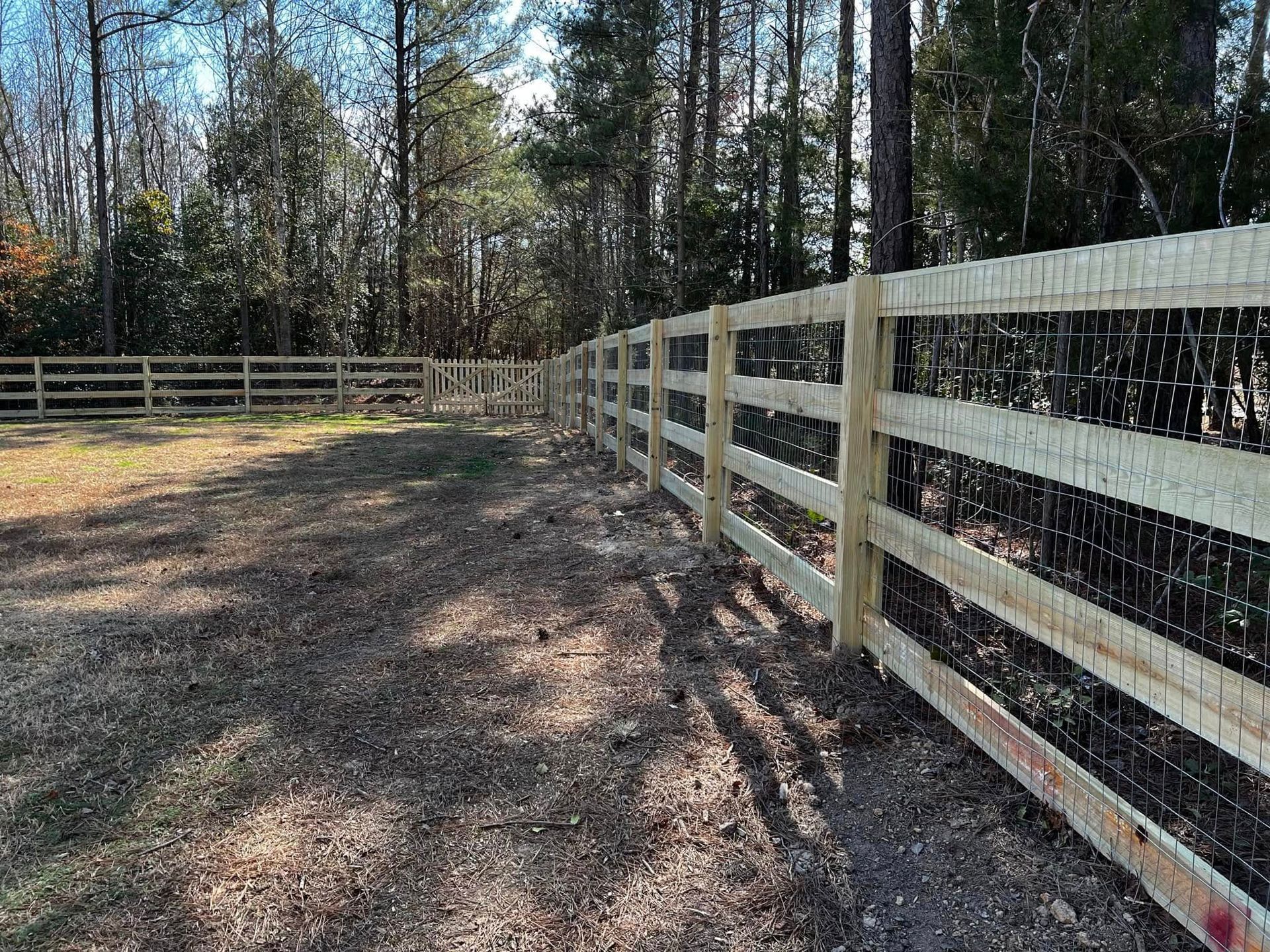 A wooden fence surrounds a dirt field with trees in the background.