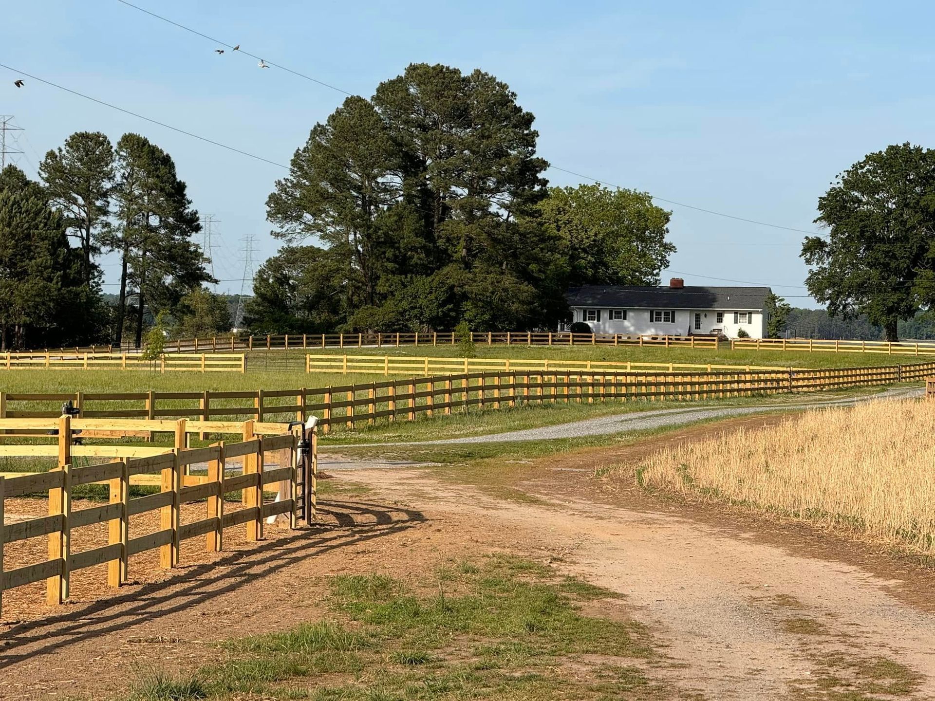 A wooden fence surrounds a grassy field with a house in the background