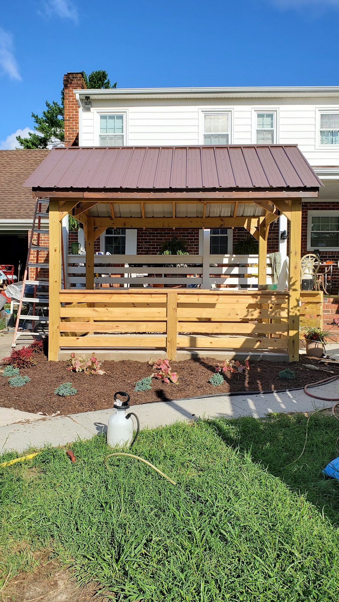A wooden gazebo is sitting in front of a house.