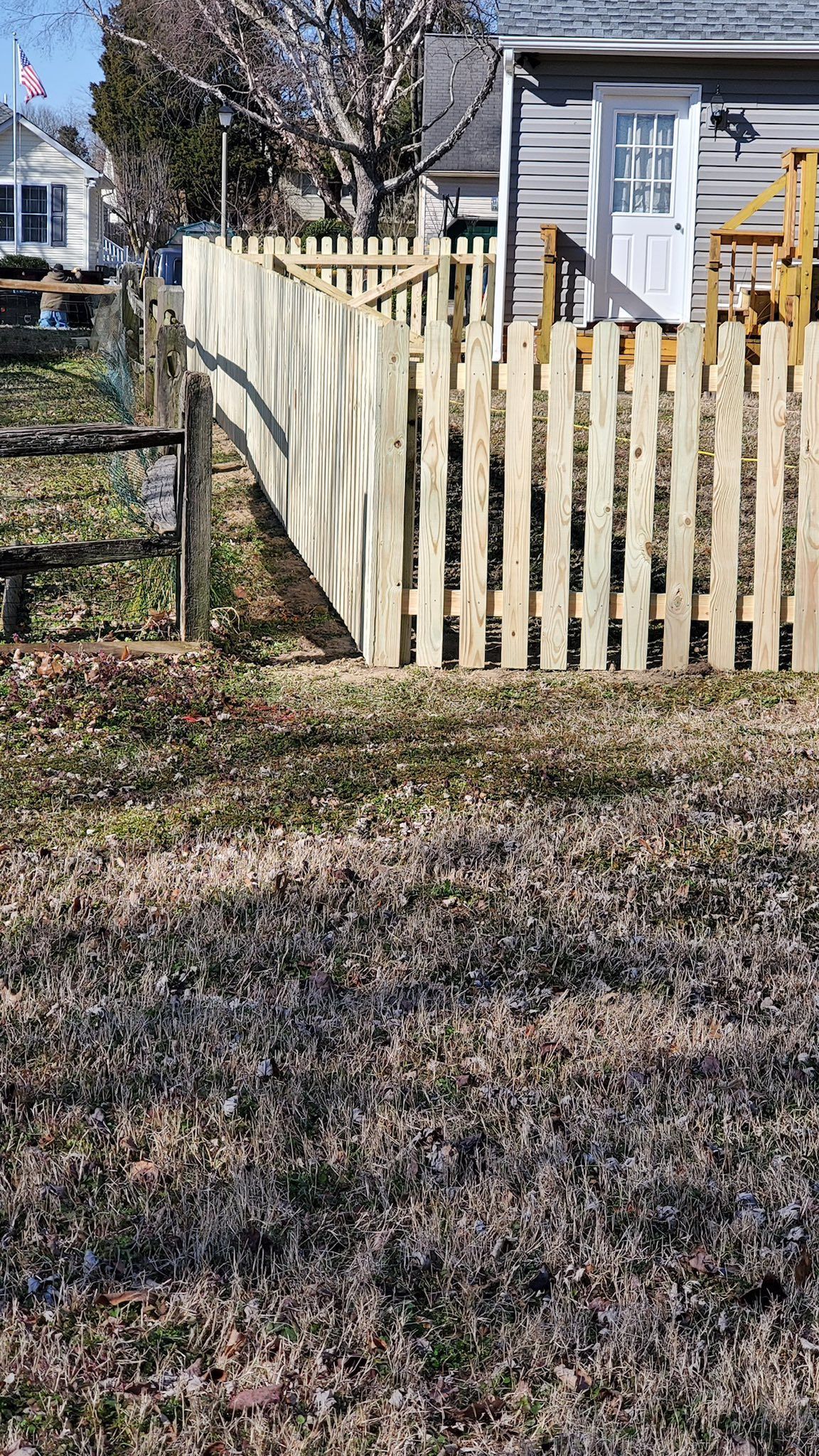 A wooden picket fence surrounds a grassy yard in front of a house.