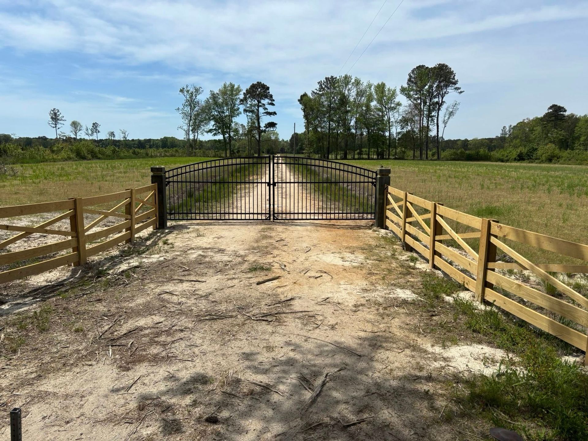 A dirt road with a wooden fence and a metal gate