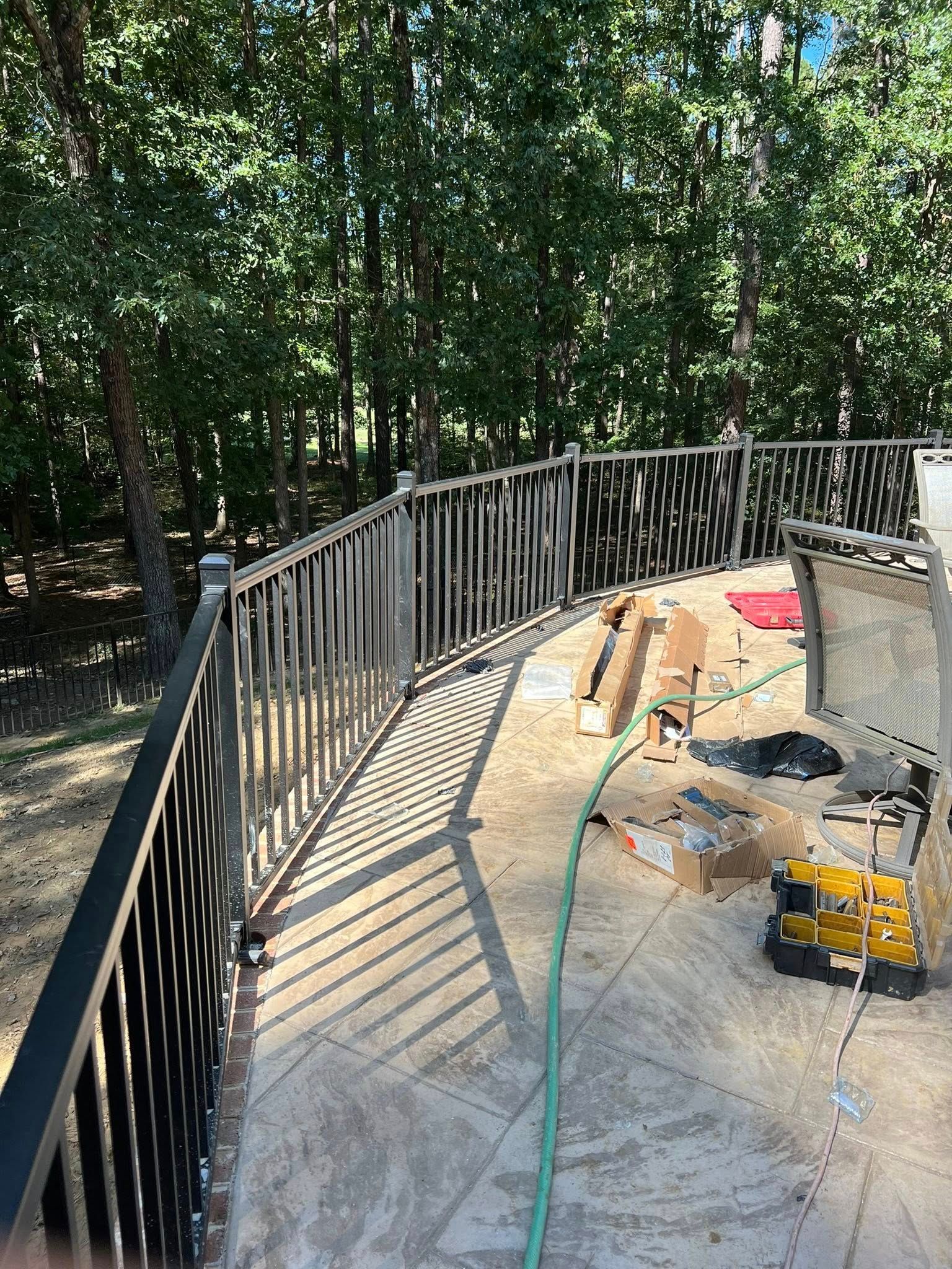 A black railing is surrounding a pool in the woods.