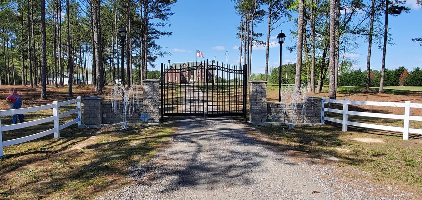 A driveway with a gate and a white fence leading to a house.