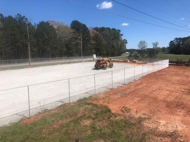 A bulldozer is driving down a dirt road next to a chain link fence.