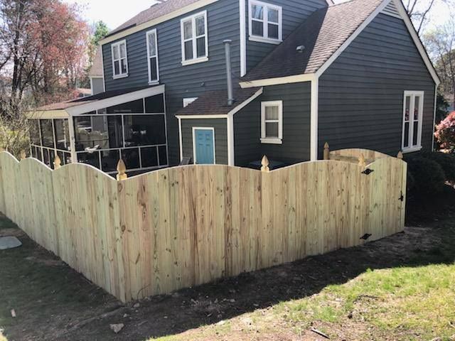 A wooden fence is in front of a house with a screened in porch.