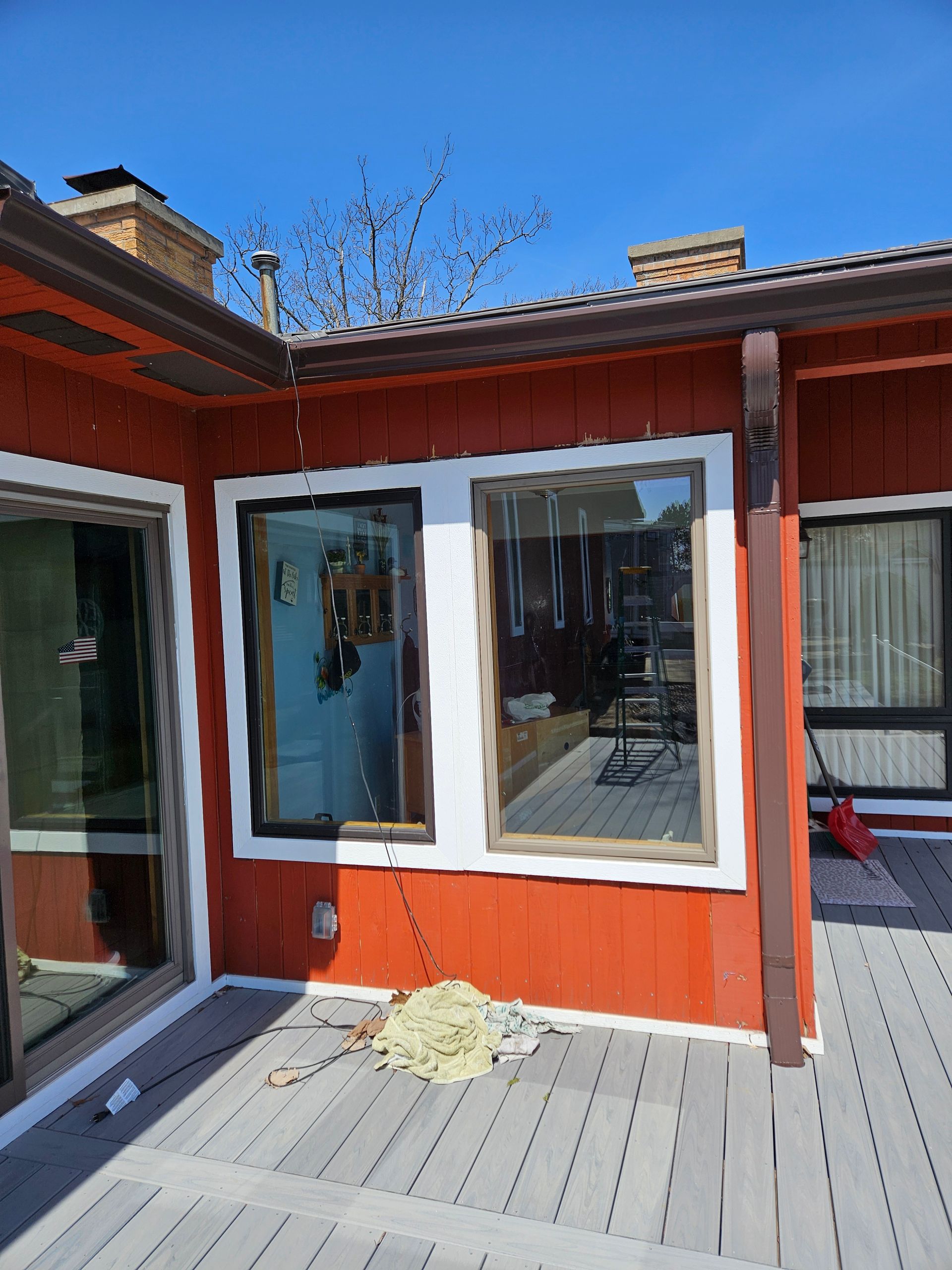 Red exterior wall with large white-trimmed window and glass door beside a gray wooden deck in sunlight