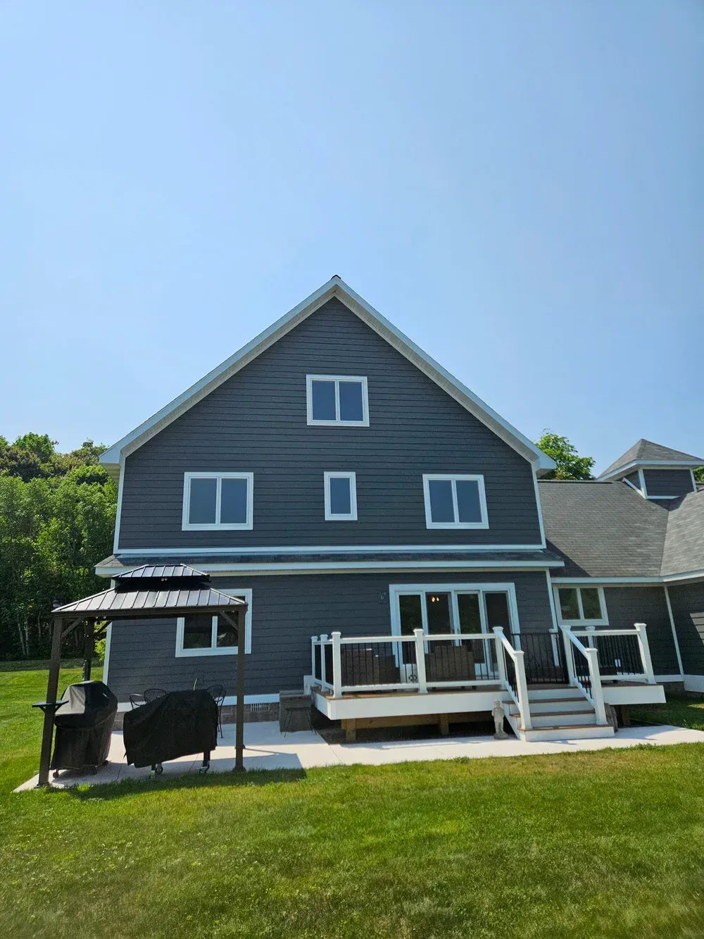 Gray house with white trim and a front porch, viewed from a grassy yard under a blue sky