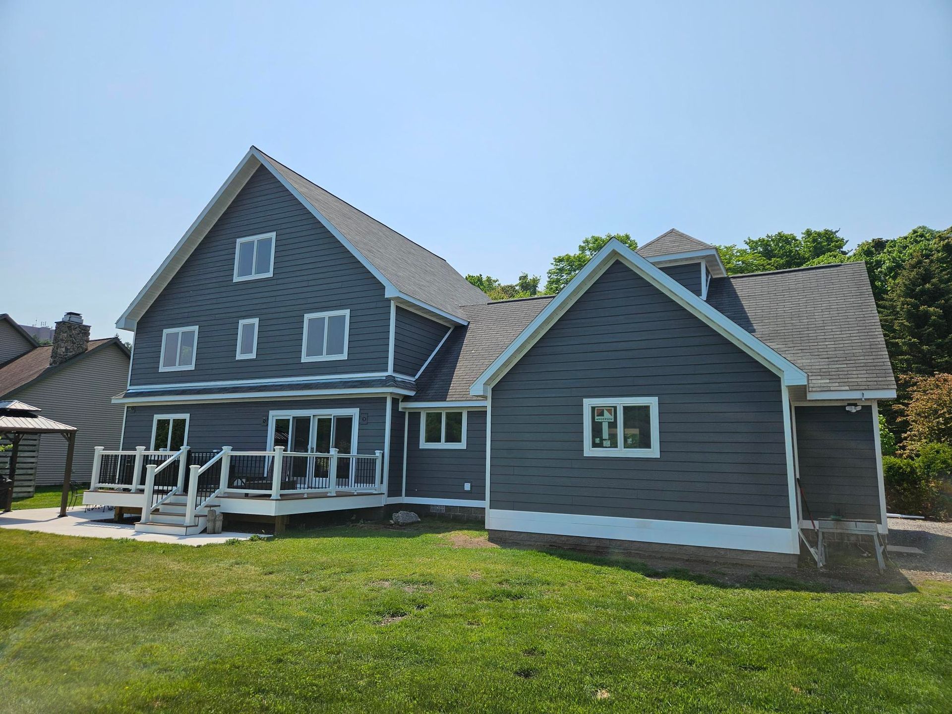 Gray house with white trim and a porch on a green lawn under a clear blue sky