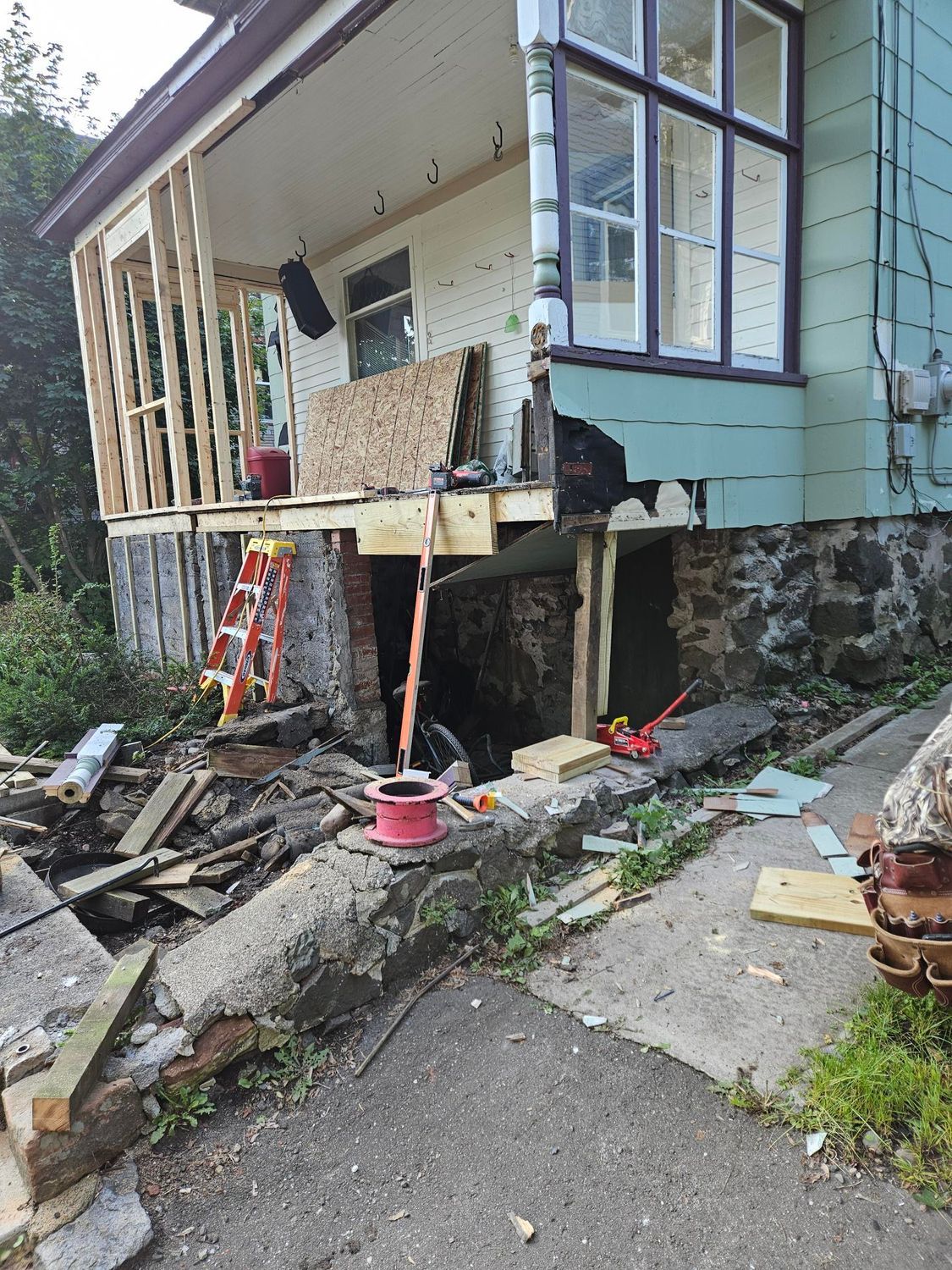 Damaged house on a slope with collapsed porch, broken stairs, and debris scattered below.