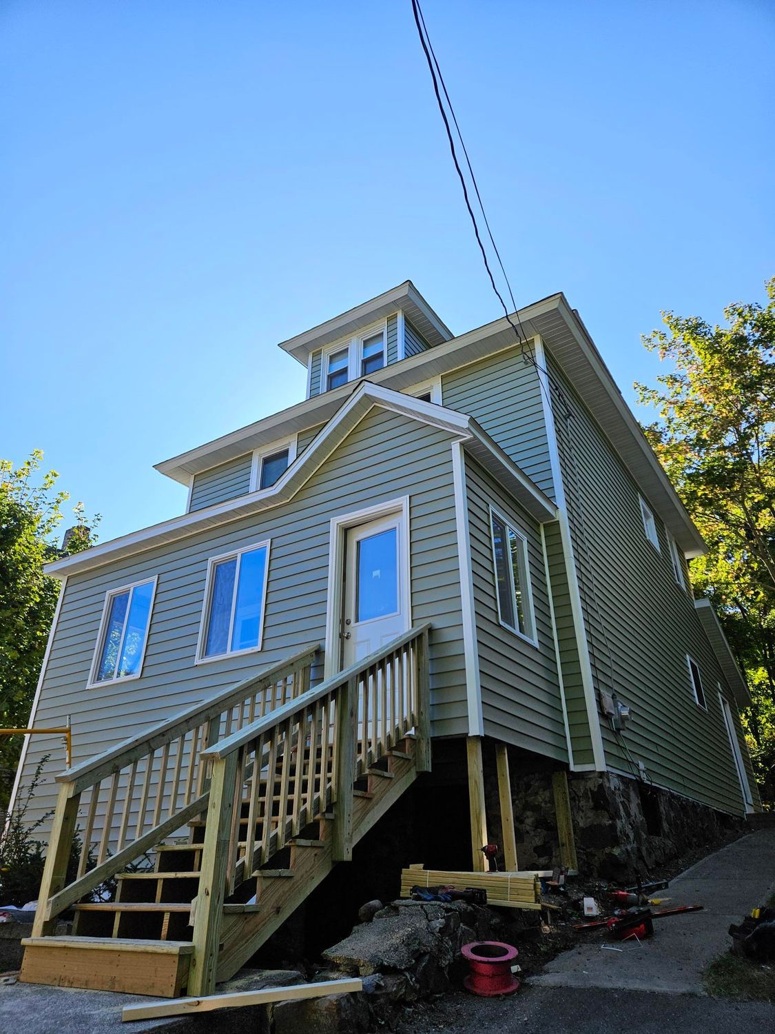 Two-story beige house with white trim and front staircase under a blue sky