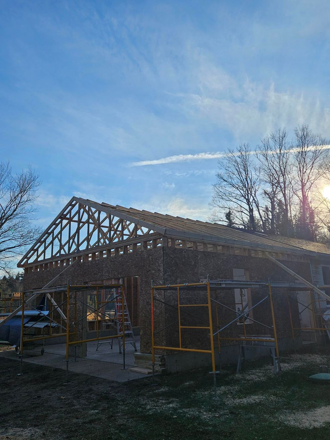 Partially built house frame with roof trusses under construction at sunset