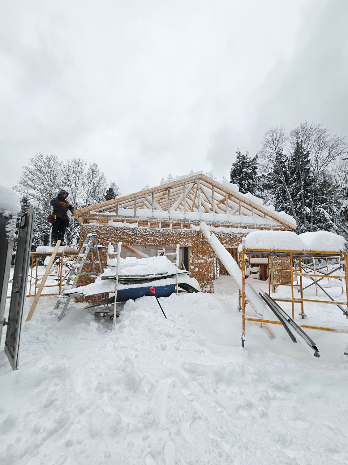 Snow-covered construction site with a wooden house frame and workers on ladders