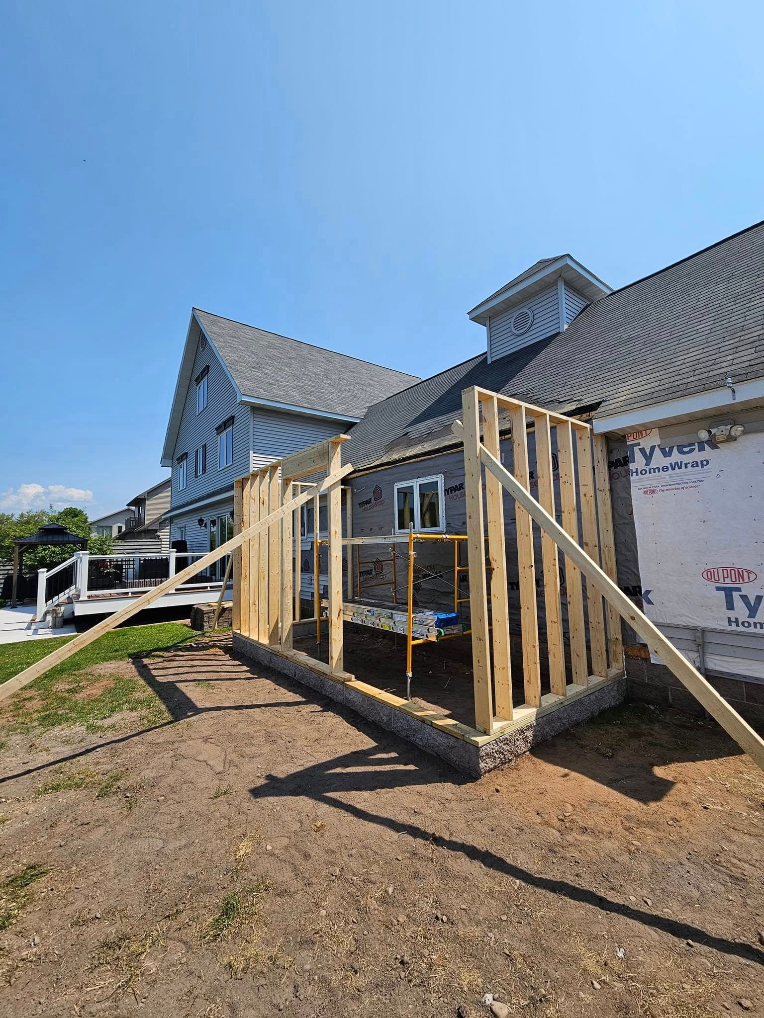 Damaged house exterior with wooden framing and debris under a clear blue sky