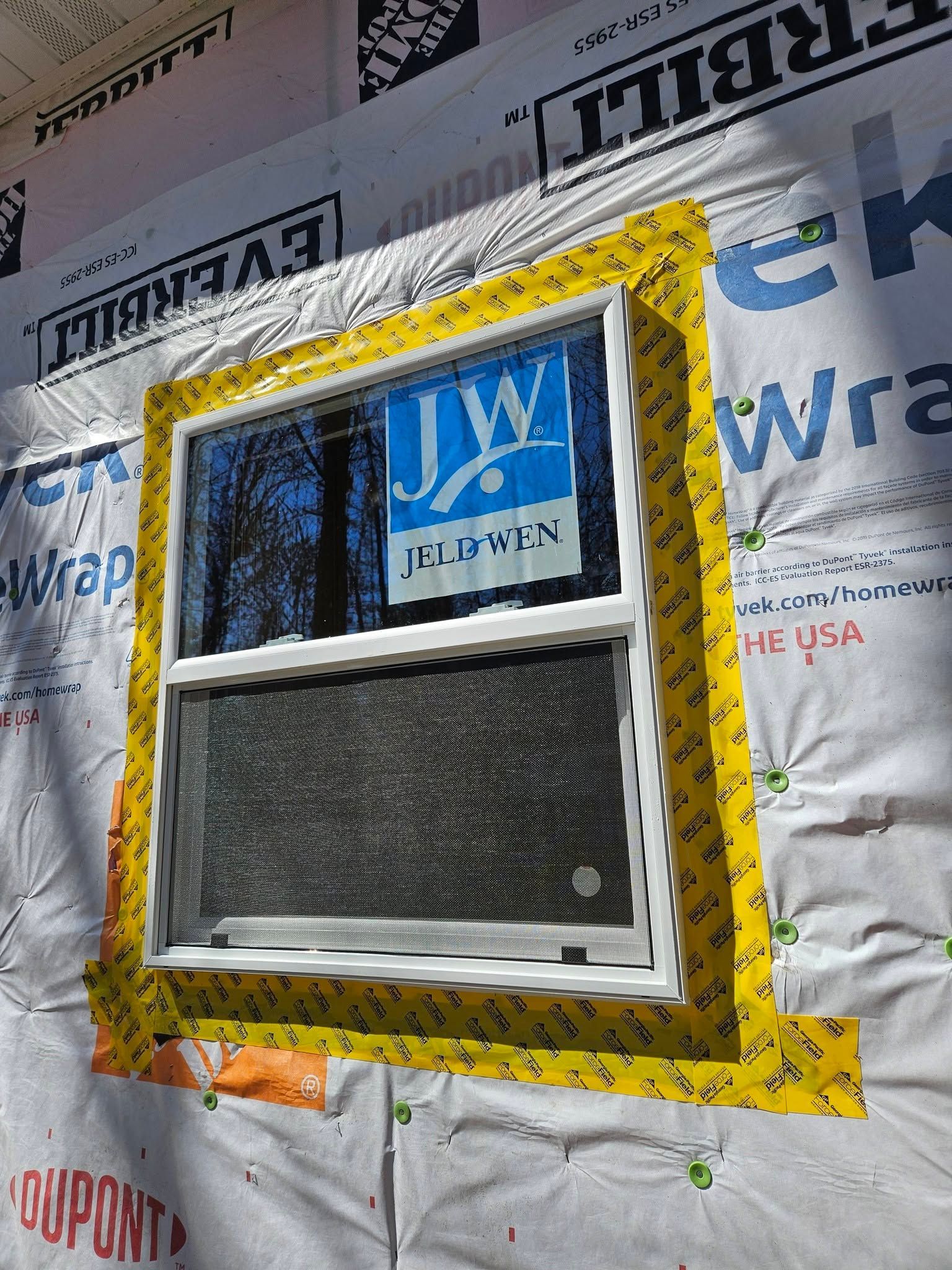 Window with yellow trim installed in a wall covered by house wrap and insulation wrap.