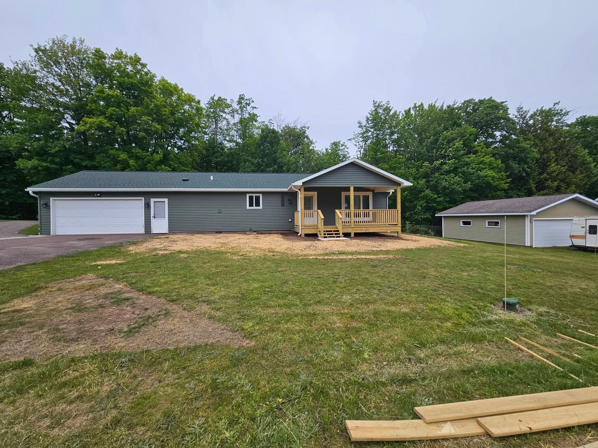 Gray house with white garage, front porch, and detached shed on a grassy yard under cloudy sky