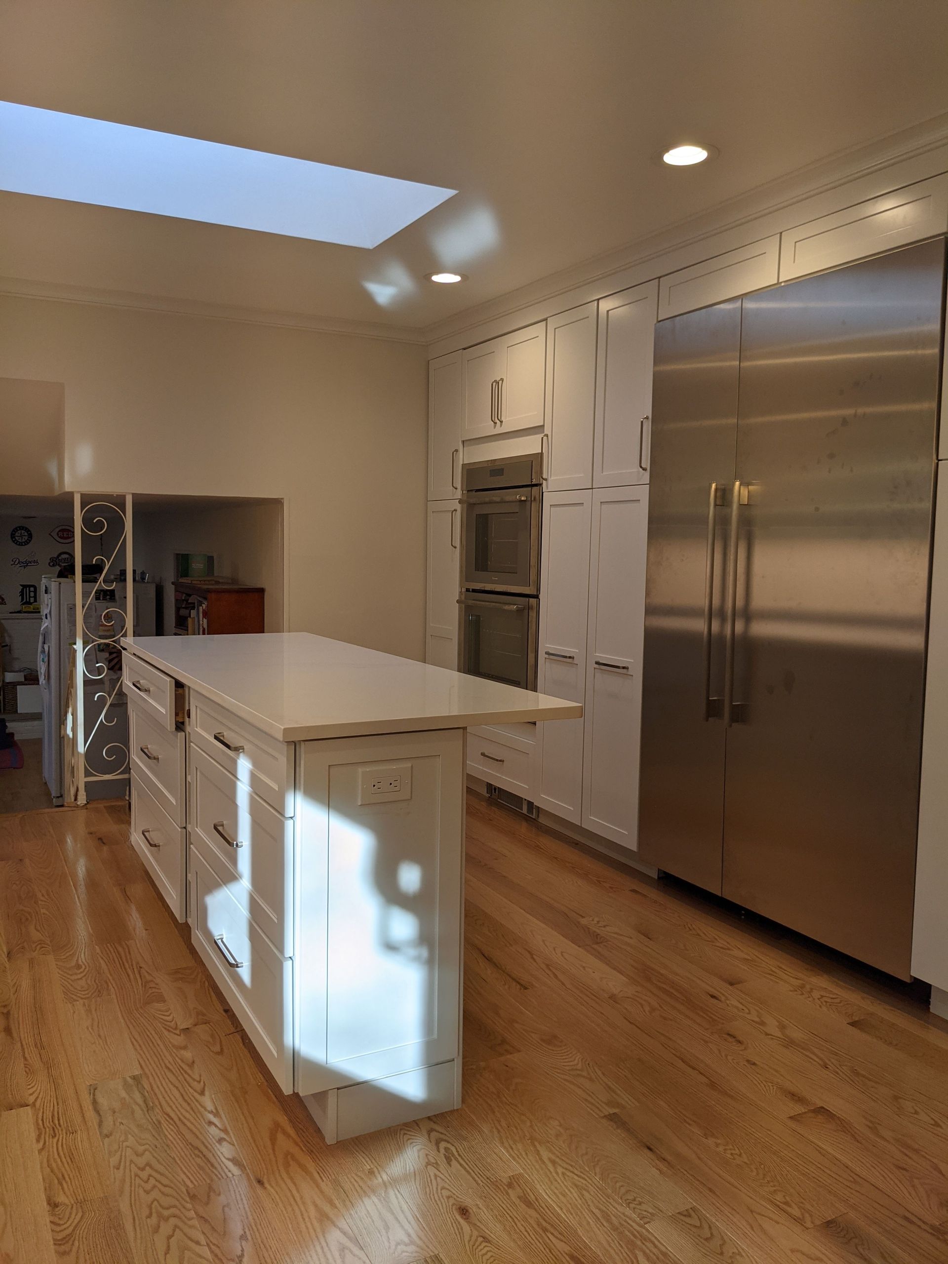 Modern kitchen with white island, stainless steel fridge, wood floors, and skylight ceiling