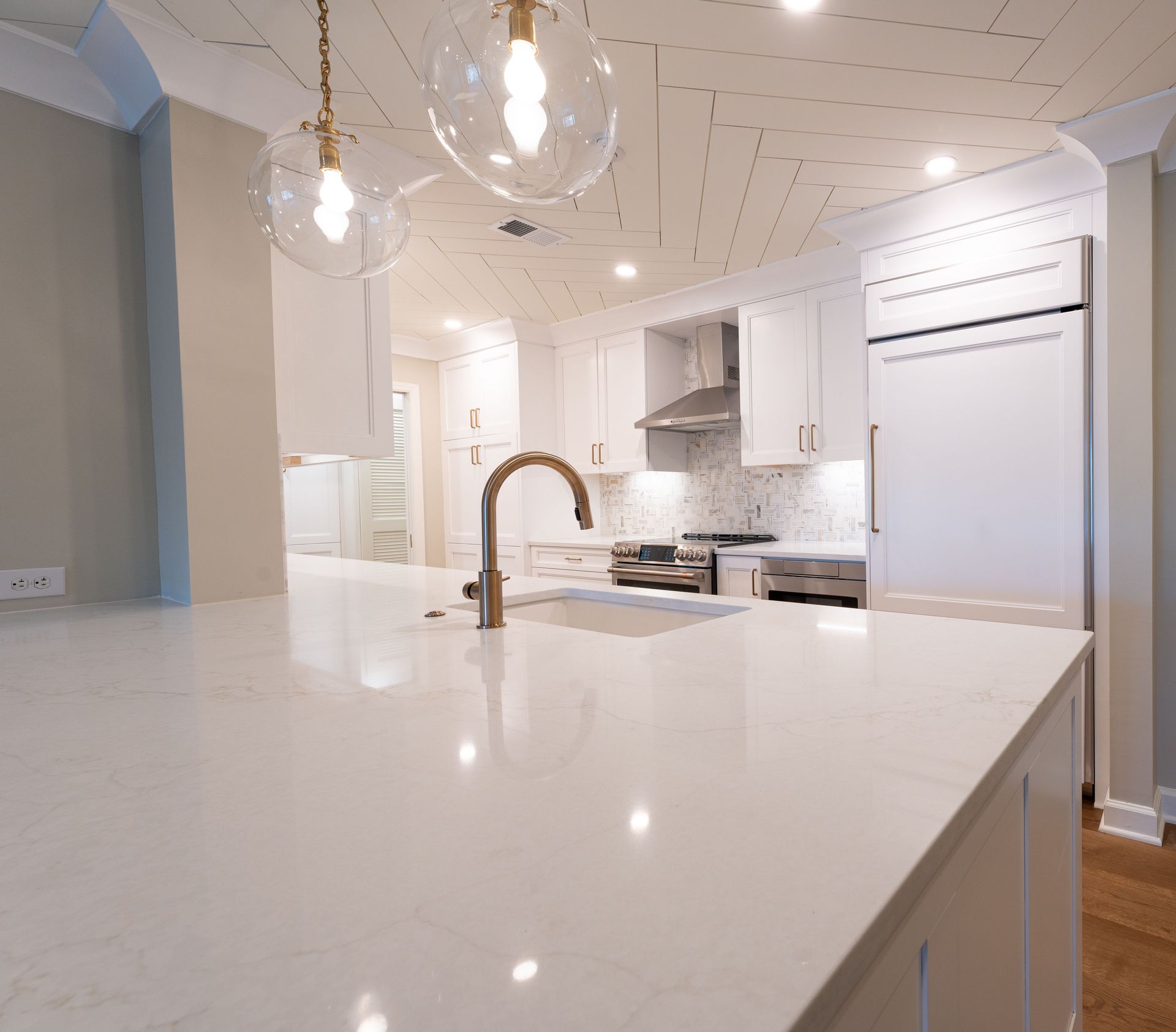 Bright white modern kitchen with large island, gold faucet, pendant lights, and stainless steel appliances