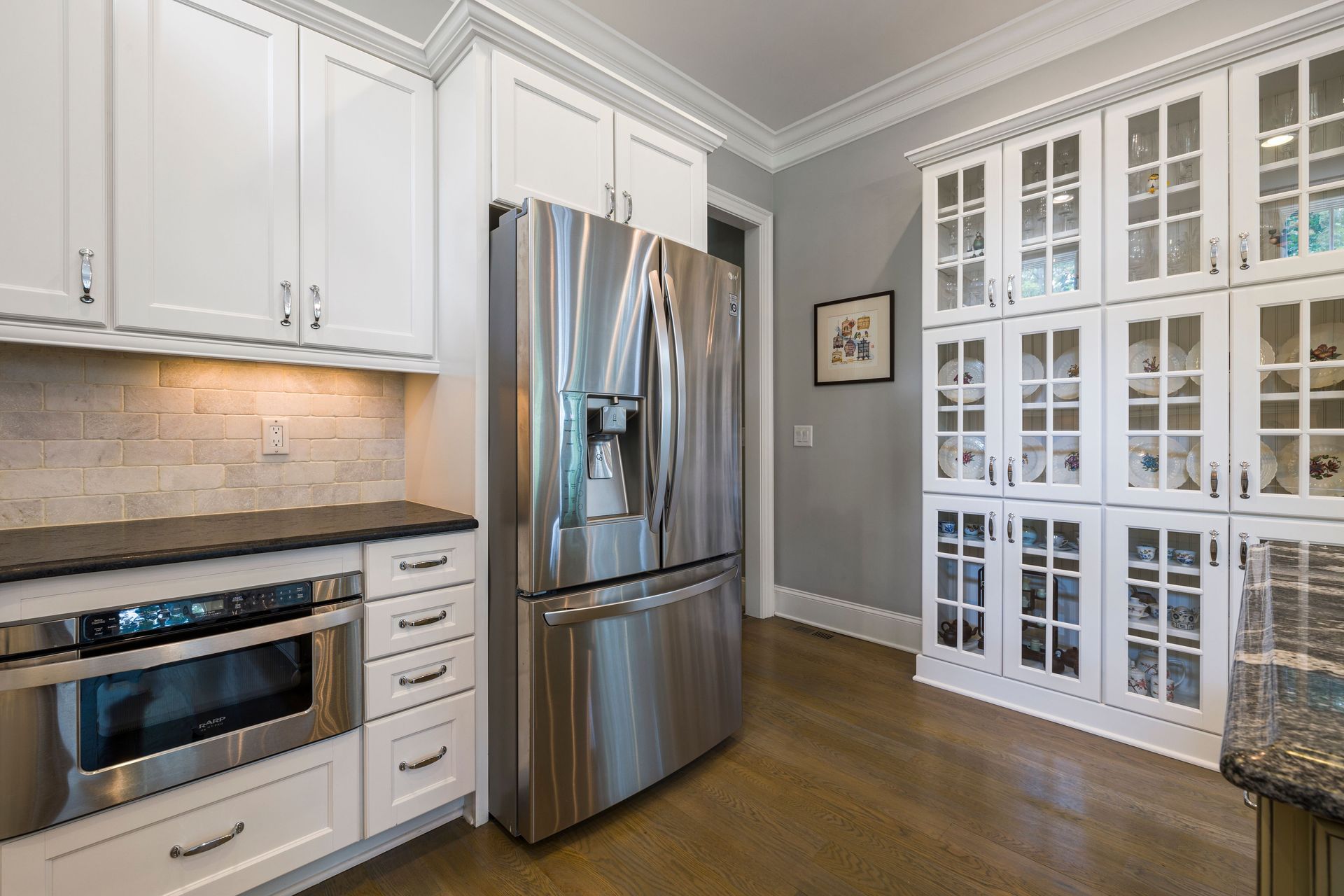 Bright kitchen with stainless steel appliances, white cabinets, and glass-front pantry doors