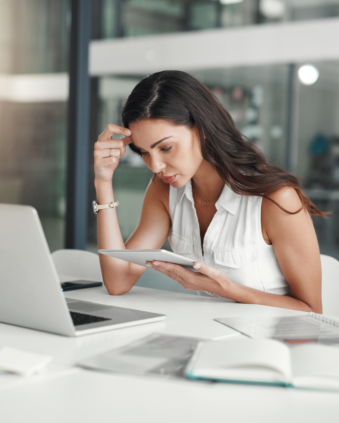 Una mujer está sentada en un escritorio con una computadora portátil y una tableta.