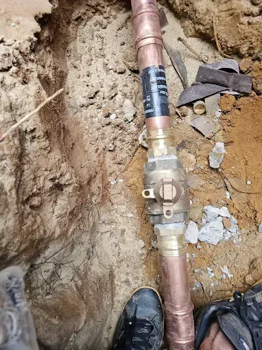 Copper pipes and valve in a trench, possibly water supply.