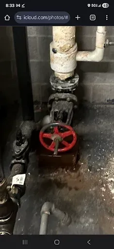 A red valve and piping in a utility room setting.