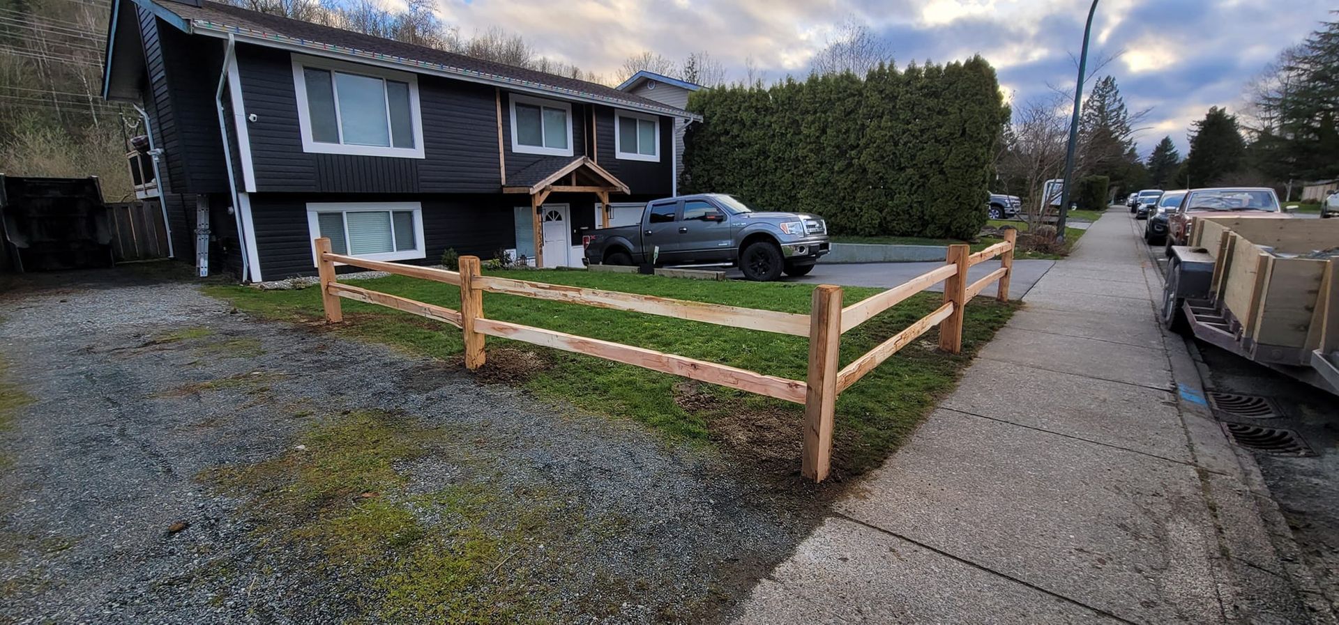 A dark two-story building with a wooden fence and a pickup truck parked in front.