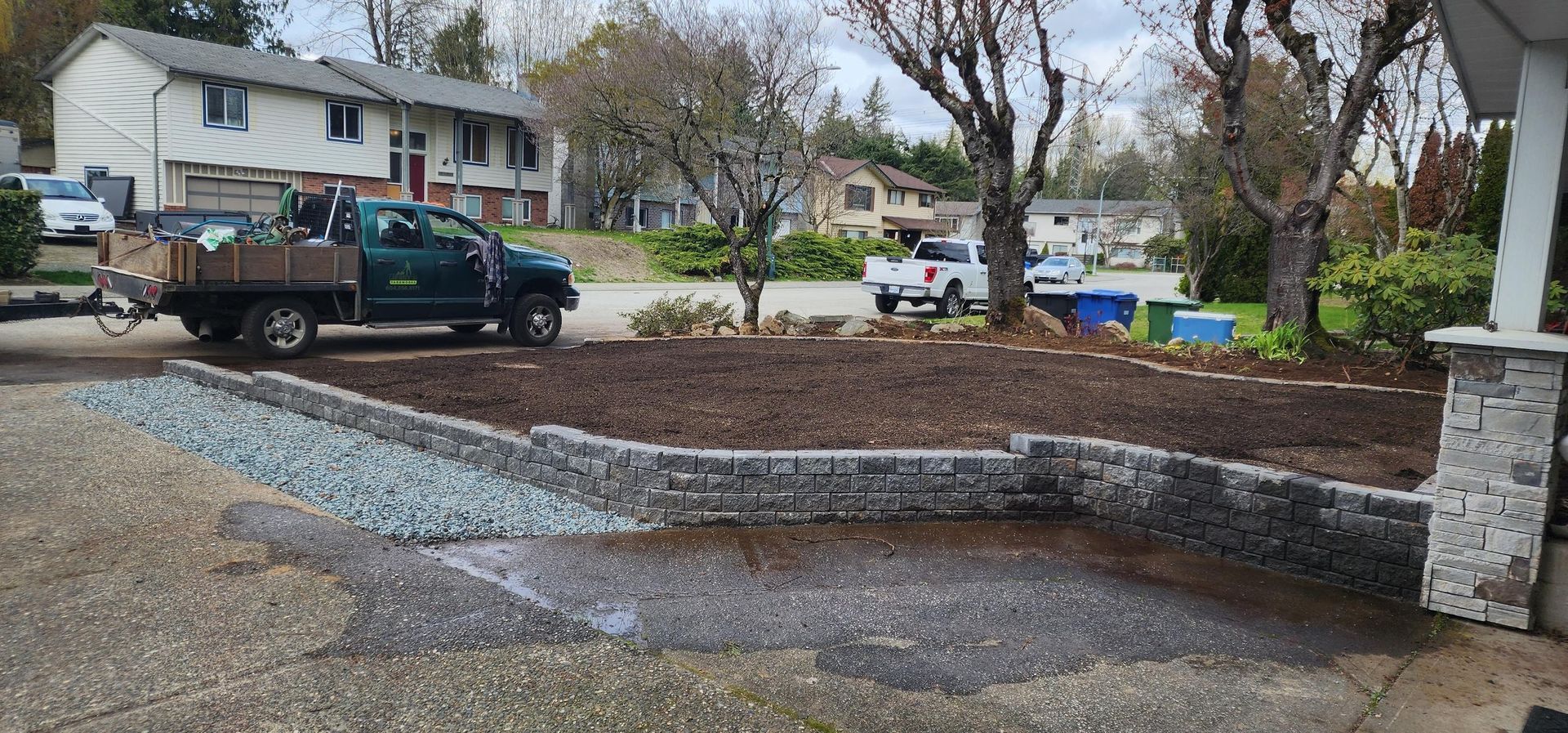 A green truck parked in front of a house, landscaping project underway with gravel and mulch.