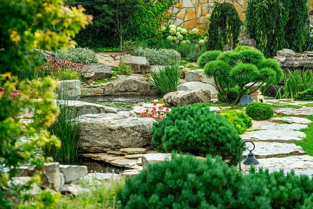 Stone garden with a pond, lush greenery, and carefully arranged rocks.