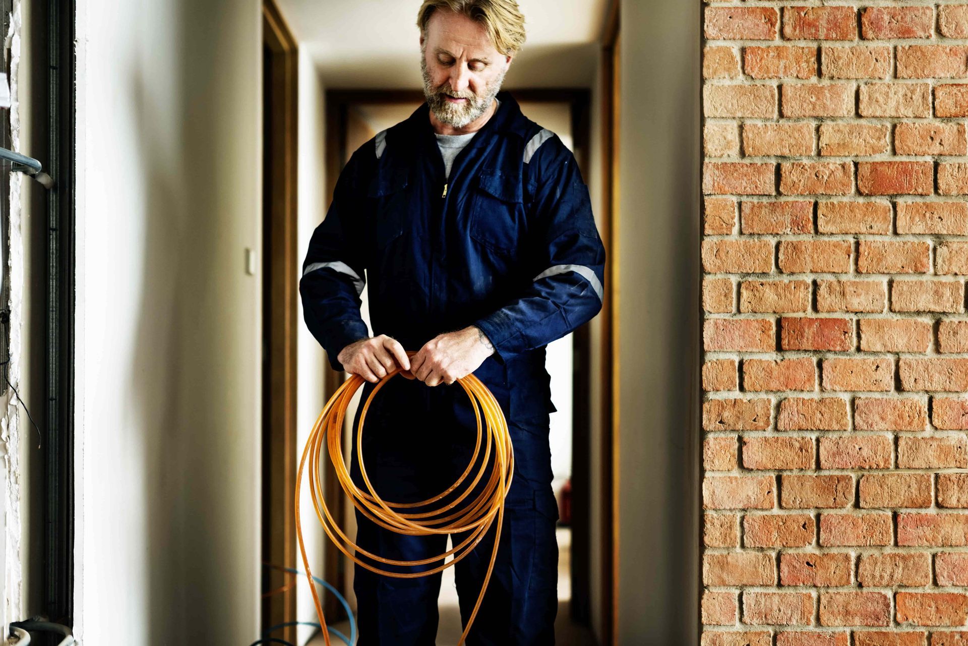 A man in a blue jumpsuit is holding a coil of orange wire.