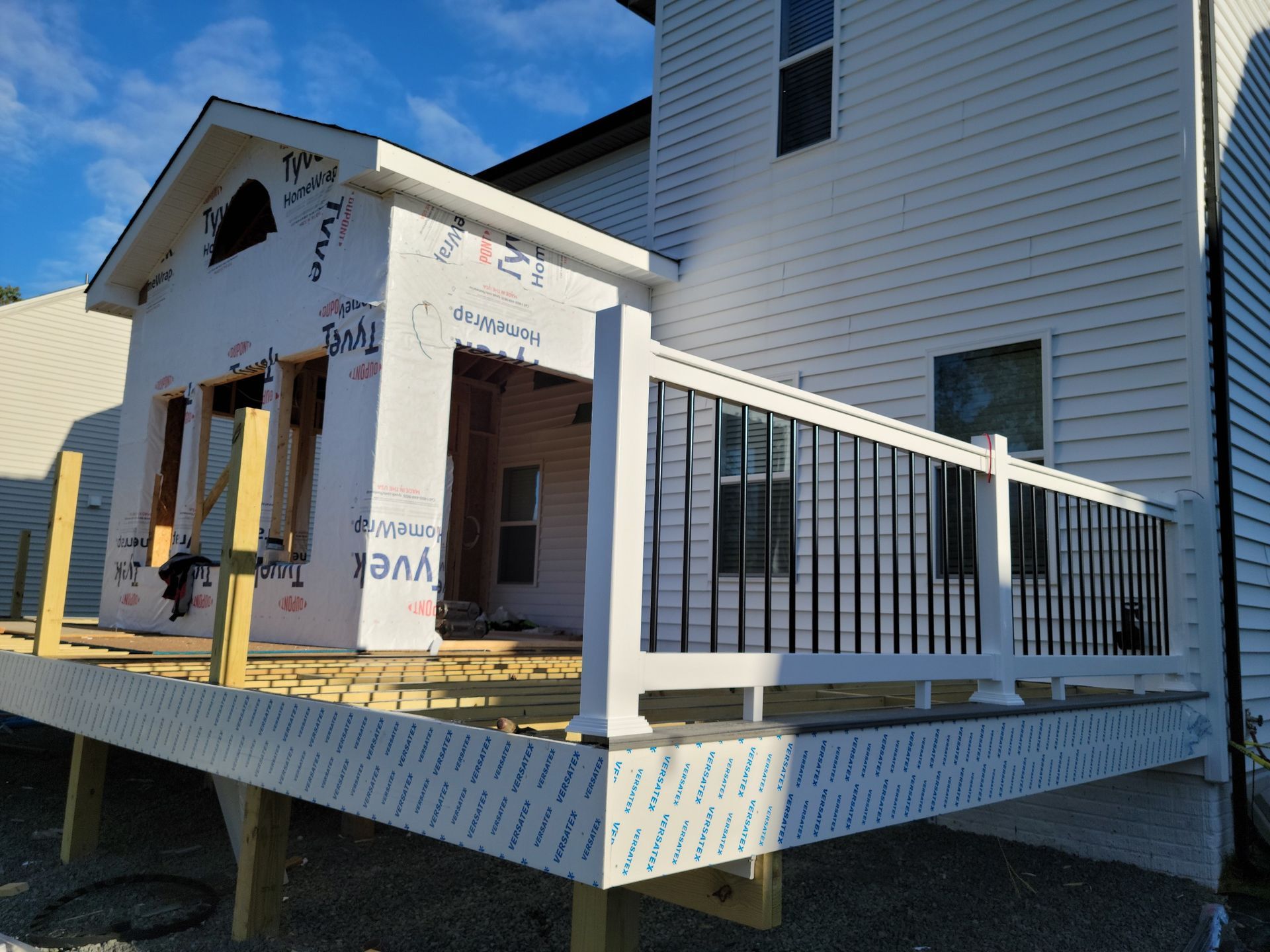 A wooden deck with white railings next to a brick building in a wooded area.