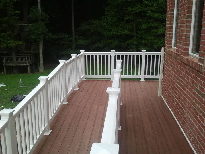 A wooden deck with white railings next to a brick building in a wooded area.