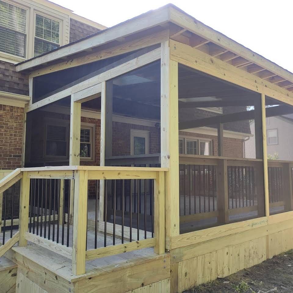Screened porch addition to a home. Light wood framing, black screening, and railings. Brick background.
