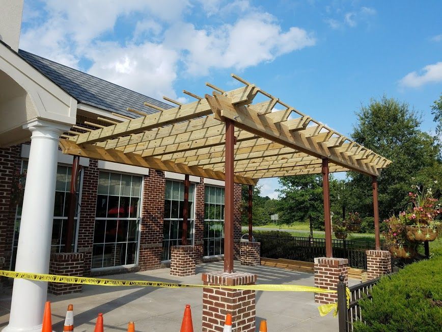 Pergola with wooden beams over a brick building's entrance, supported by columns; caution tape, cones present.