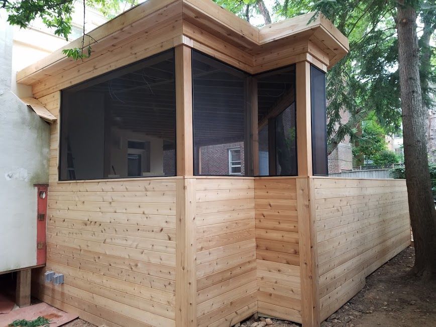 Screened-in wooden porch addition with horizontal siding, next to a tree.
