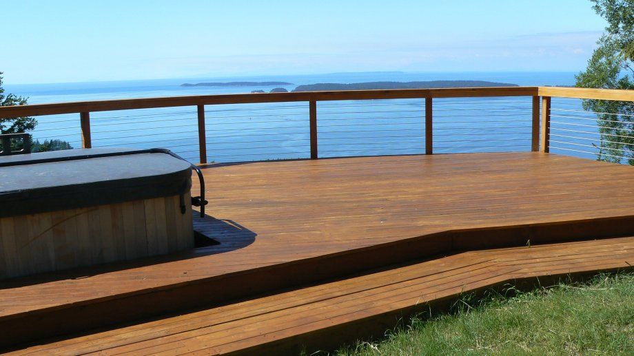 Wooden deck with hot tub, overlooking a blue lake and horizon.