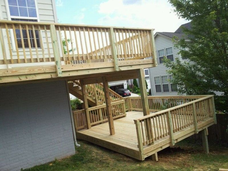Wooden multi-level deck attached to a house, with stairs and railings, set on a grassy slope.