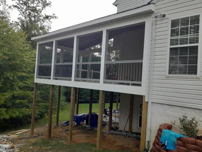 Screened-in porch elevated on wooden posts, attached to a white house with a brick foundation.