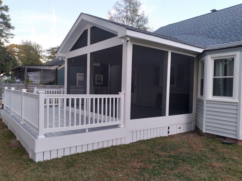 White screened porch attached to a light blue house with a gray shingled roof.  A white deck is in front.