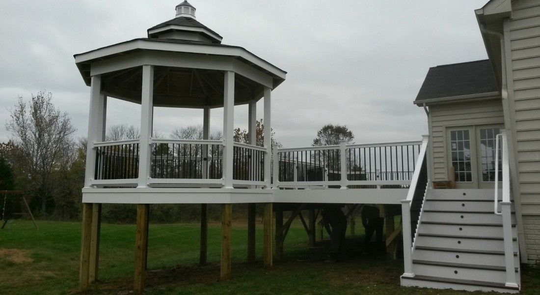 White gazebo on elevated deck, attached to a house with a staircase; overcast sky.