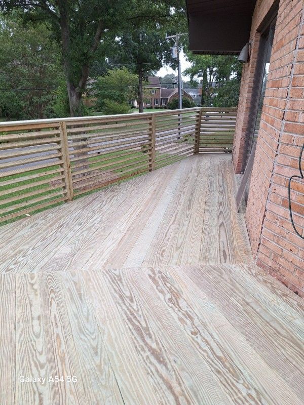 Wooden deck with slatted railing against a brick wall.