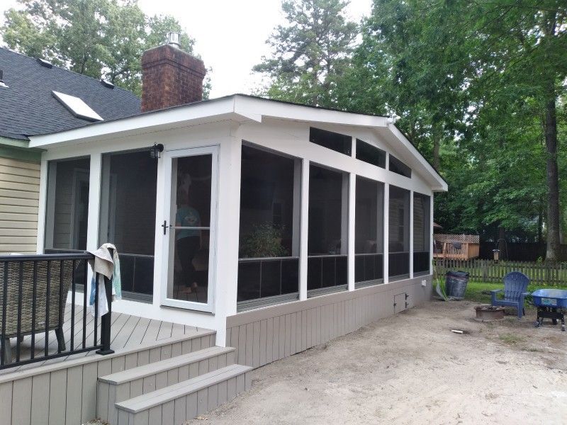 Screened-in porch addition with white trim, gray siding, and deck stairs. Backyard setting, trees in background.