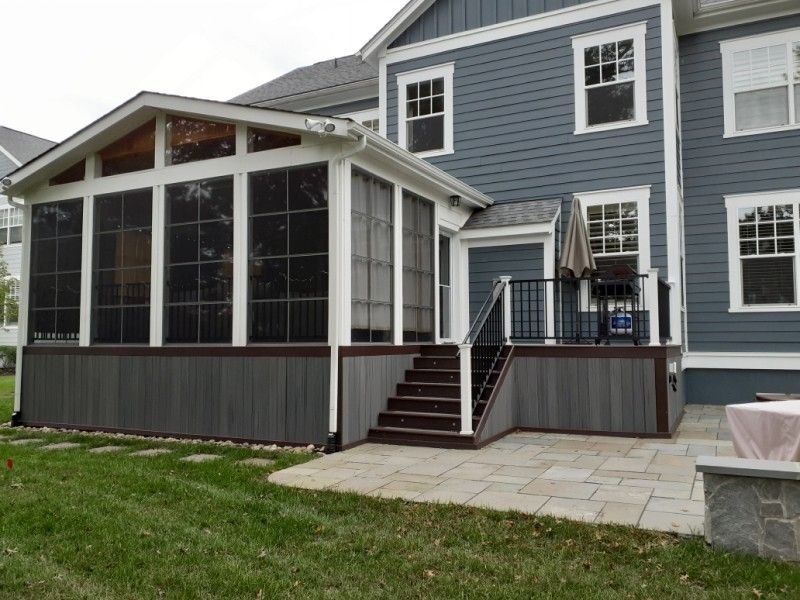 Gray screened-in porch with steps and deck connected to a blue house with white trim.