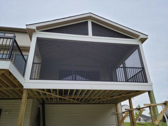 Screened-in porch on a wooden deck, brown screen, white trim, black railing, attached to a beige house, cloudy sky.