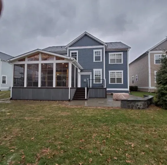 Back view of a two-story blue house with a screened porch, deck, and a backyard on a cloudy day.