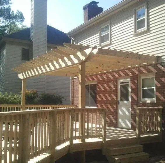 Wooden deck with pergola attached to a brick house.