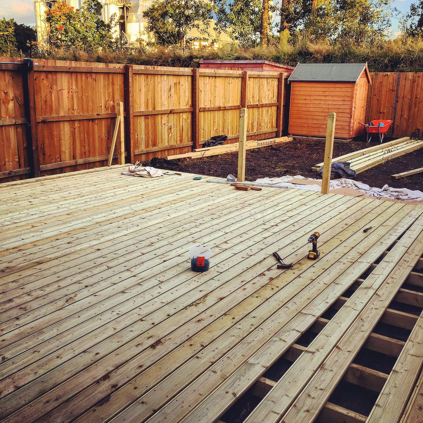 Wooden deck under construction, with tools, lumber, and shed visible, in a backyard setting.